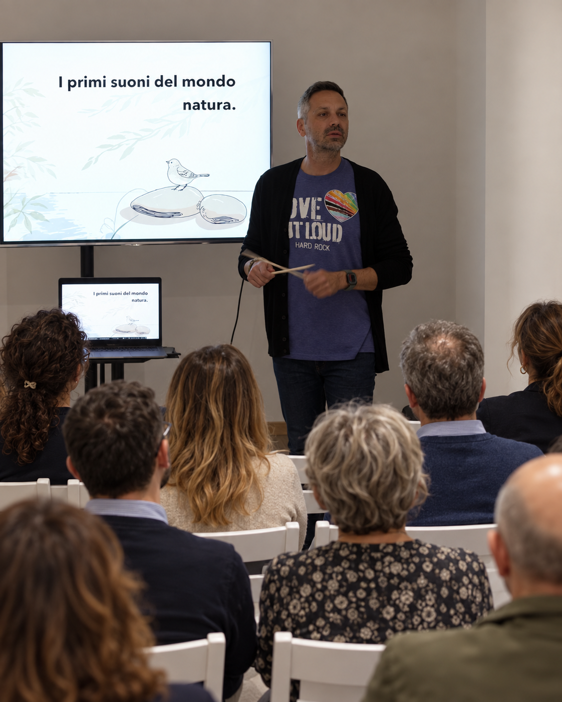 Armando Cacciato davanti a un pubblico adulto durante una presentazione sulla musica, immagine rielaborata